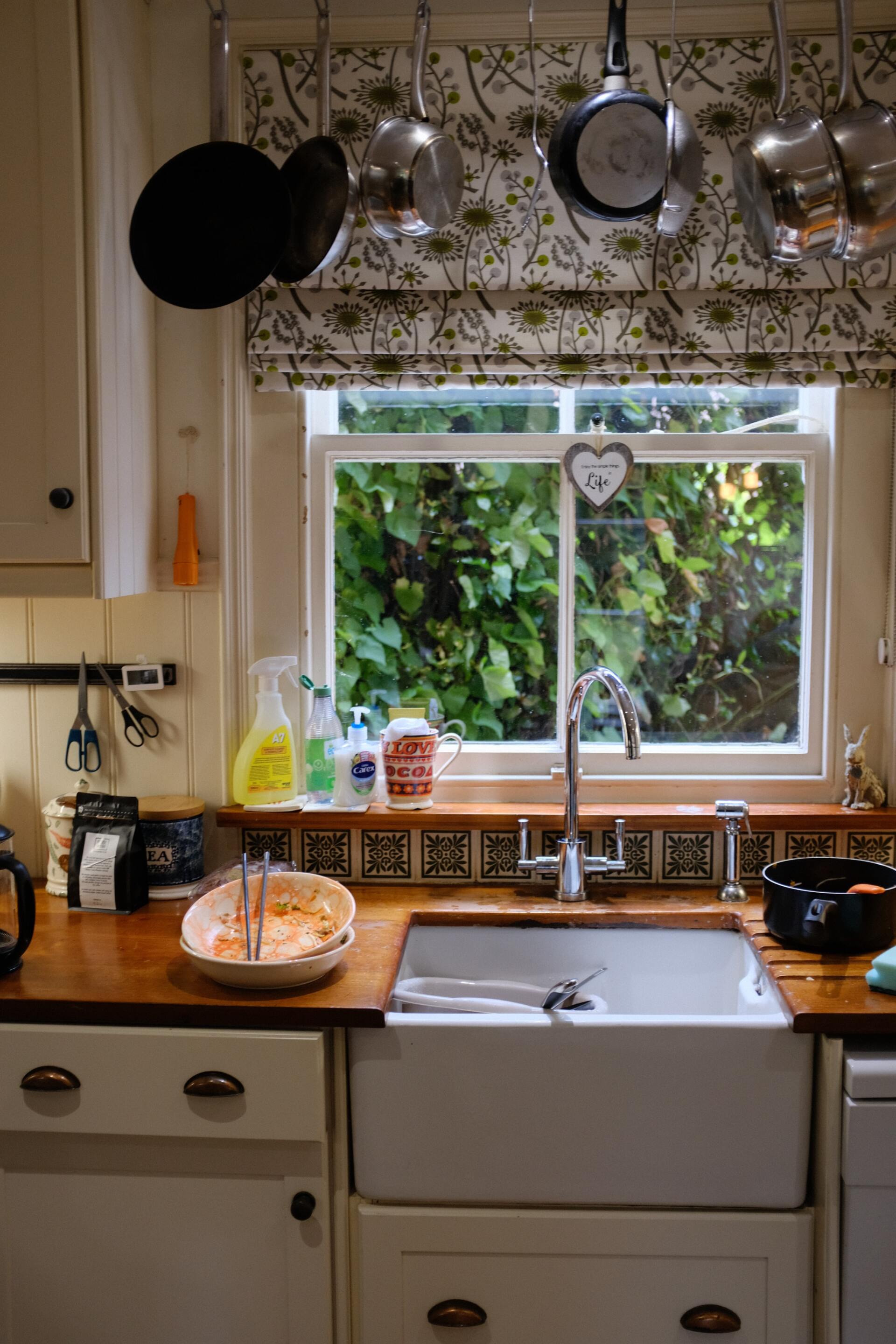 A kitchen with a sink and a window with pots and pans hanging from the ceiling | plumbing emergency service near me