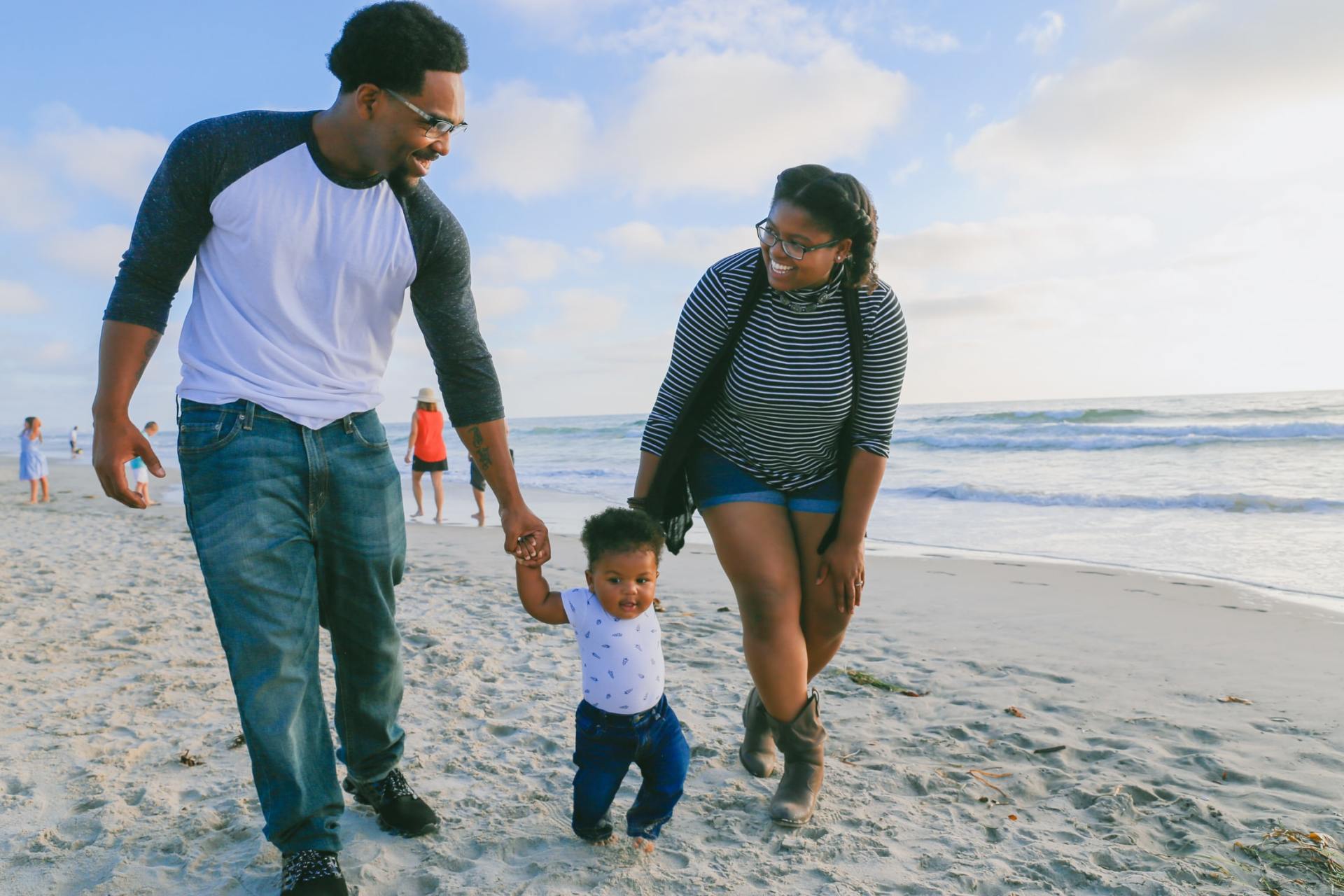 Parents walk hand-in-hand with their toddler along a sandy beach at sunset.
