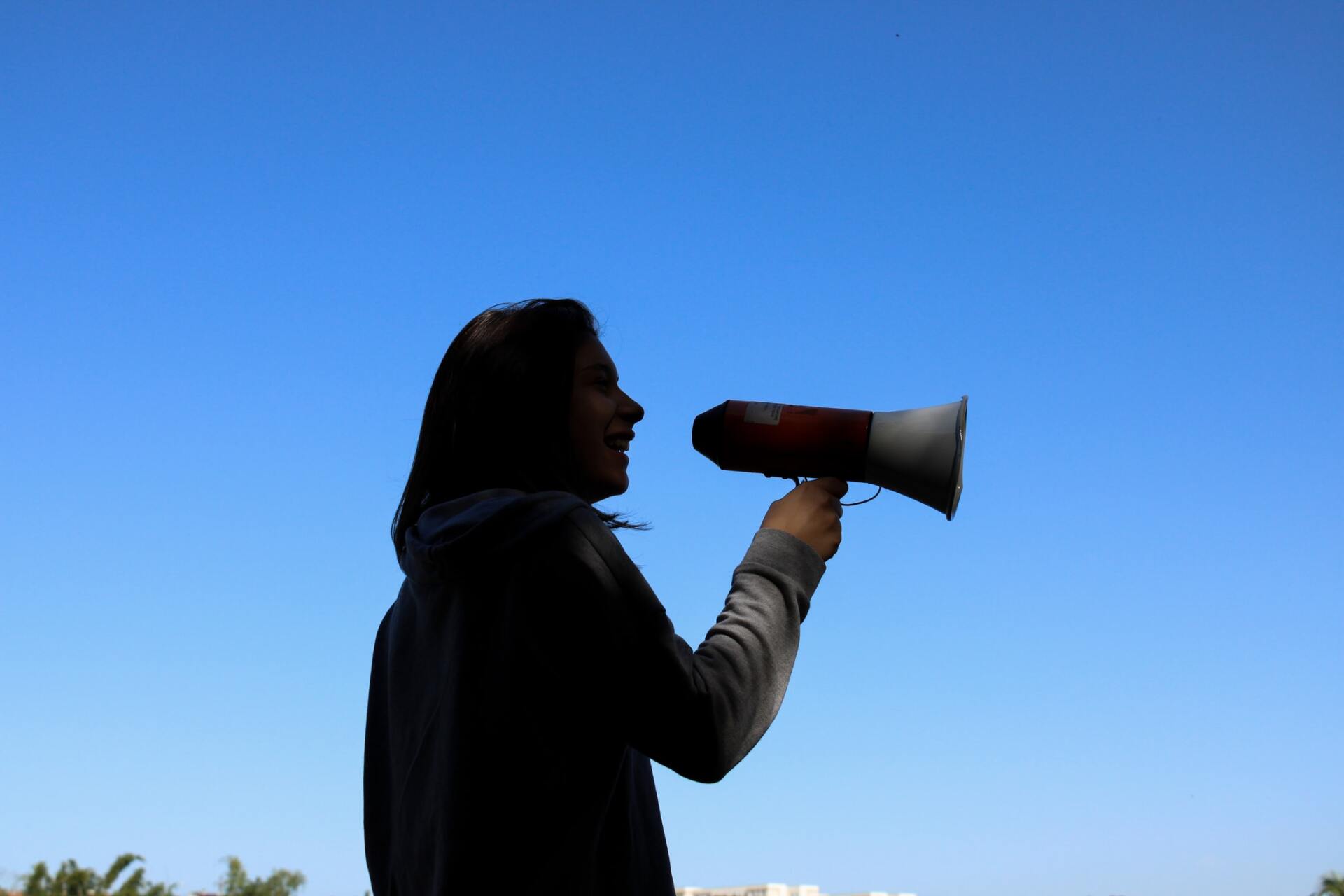 A woman is holding a megaphone in front of a blue sky