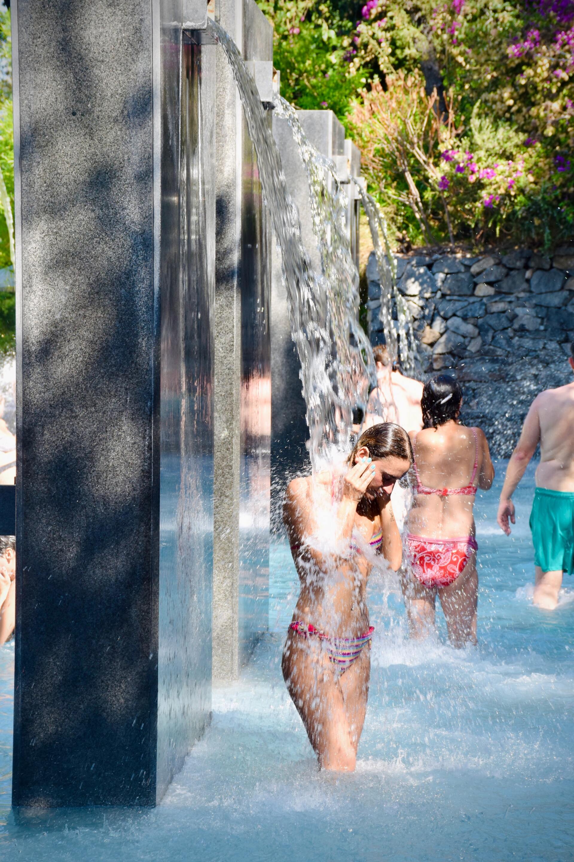 Menschen kühlen sich unter einer Wasserwand in einem Freibadbereich ab