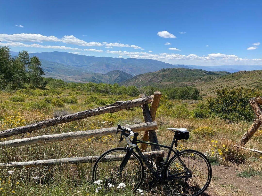 A bicycle is leaning against a wooden fence in a field with mountains in the background.
