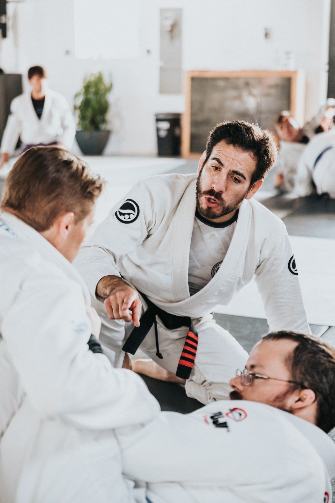 Martial arts students in white gis practicing grappling on a mat in a bright studio