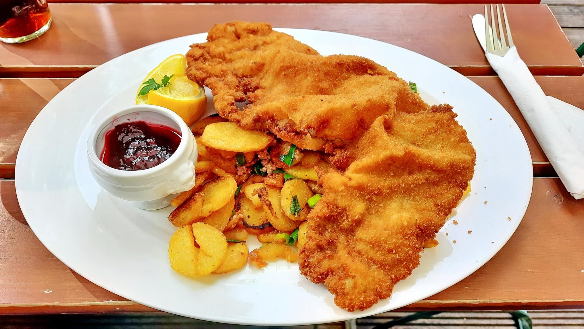 Paniertes Schnitzel mit Kartoffelscheiben und roter Soße auf einem weißen Teller