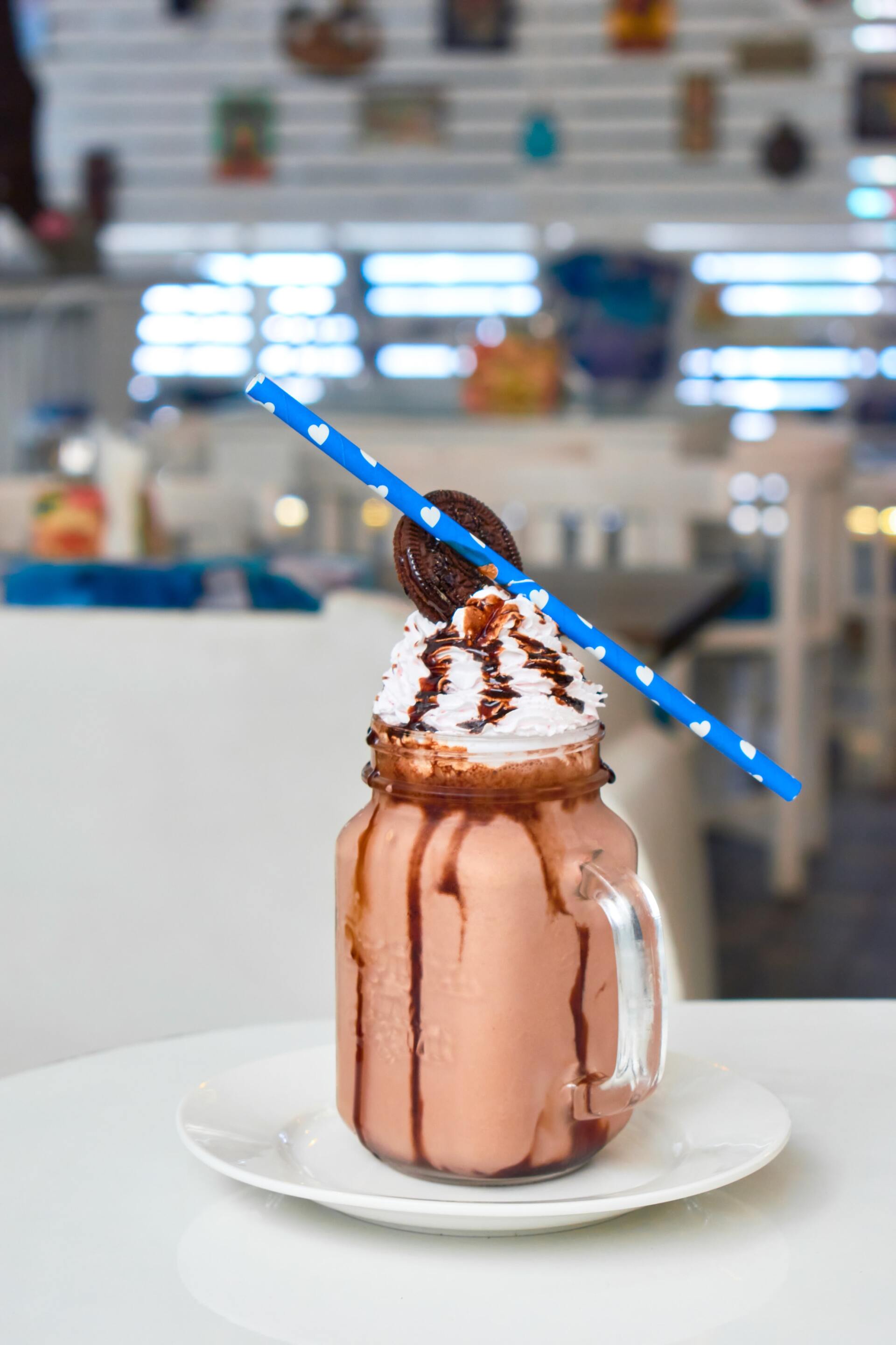 A milkshake with whipped cream and a cookie on top is on a plate on a table.