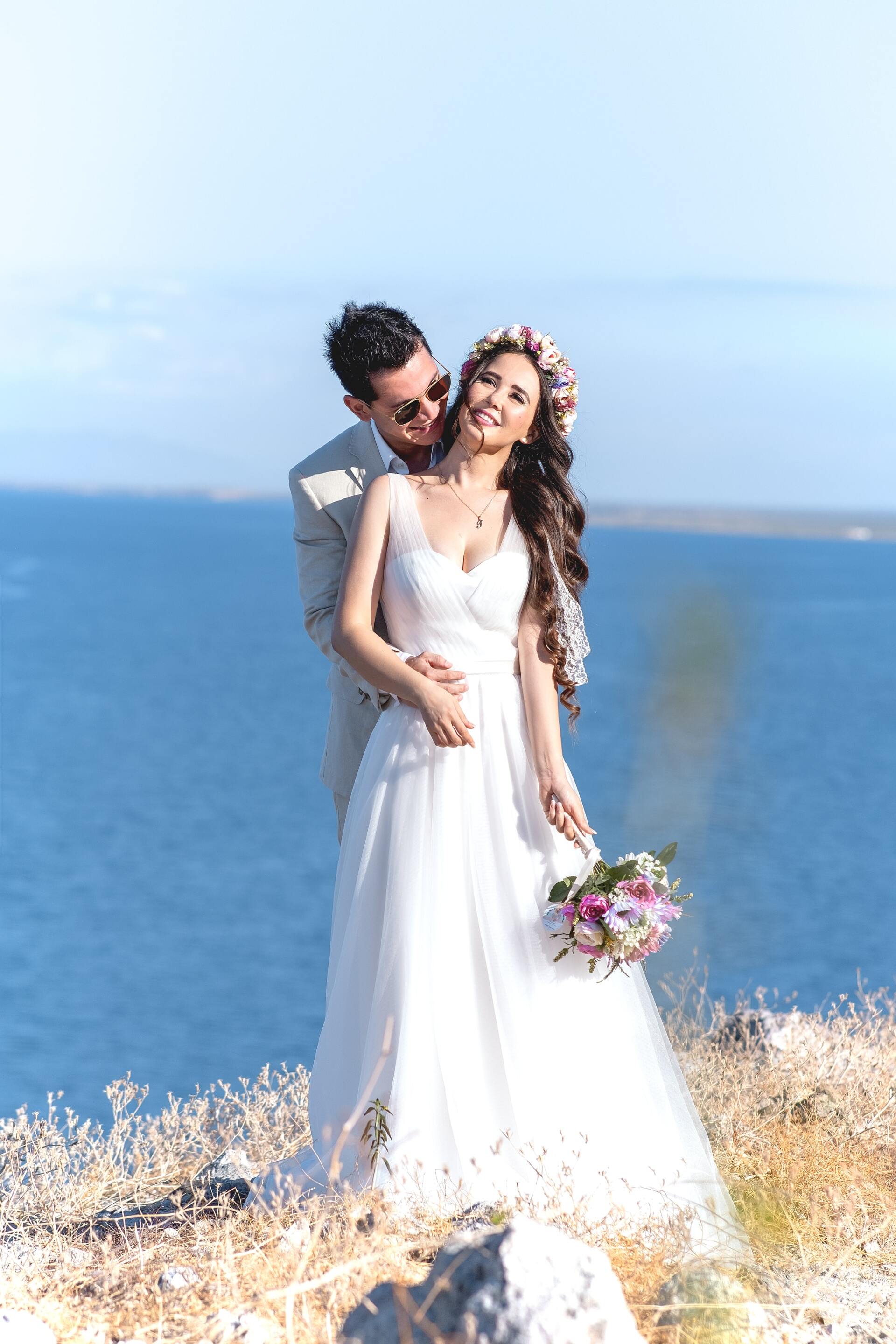 Una novia y un novio posan para una foto en un acantilado con vistas al océano.
