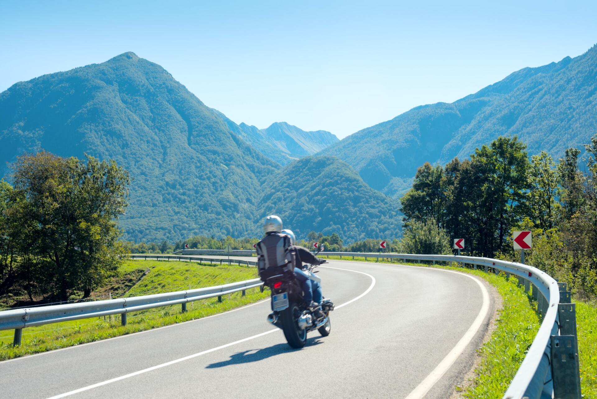 Motorrad auf einer kurvenreichen Bergstraße mit blauen Gipfeln und einer Leitplanke unter klarem Himmel