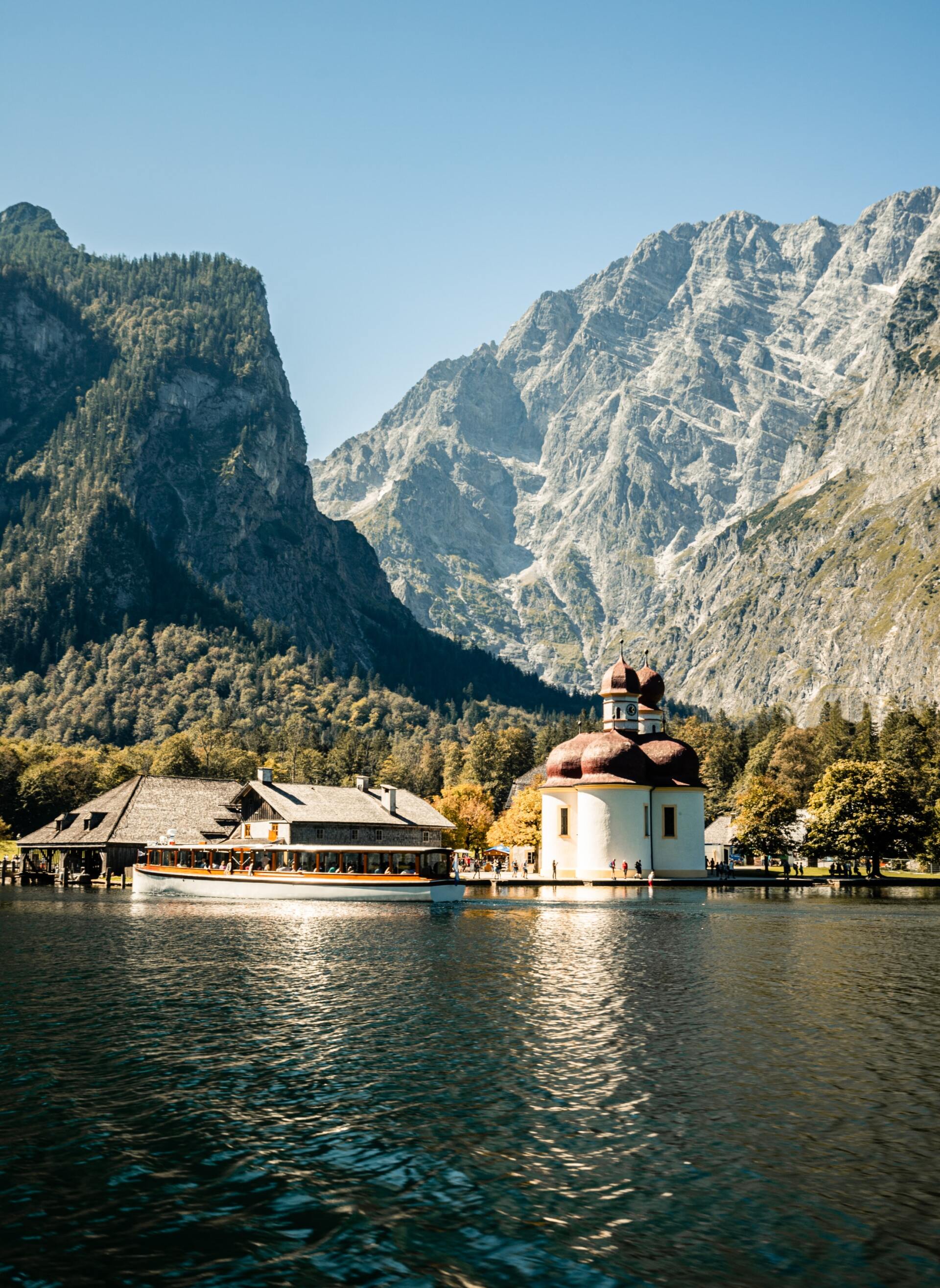 Bergsee mit einer weißen Kirche und Gebäuden am Ufer, im Hintergrund steile Felsgipfel
