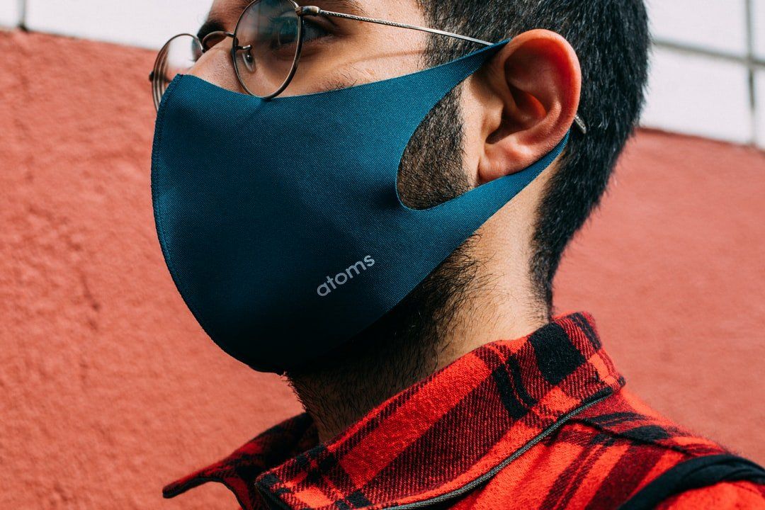 A man wearing a blue face mask and glasses is standing in front of a red wall.