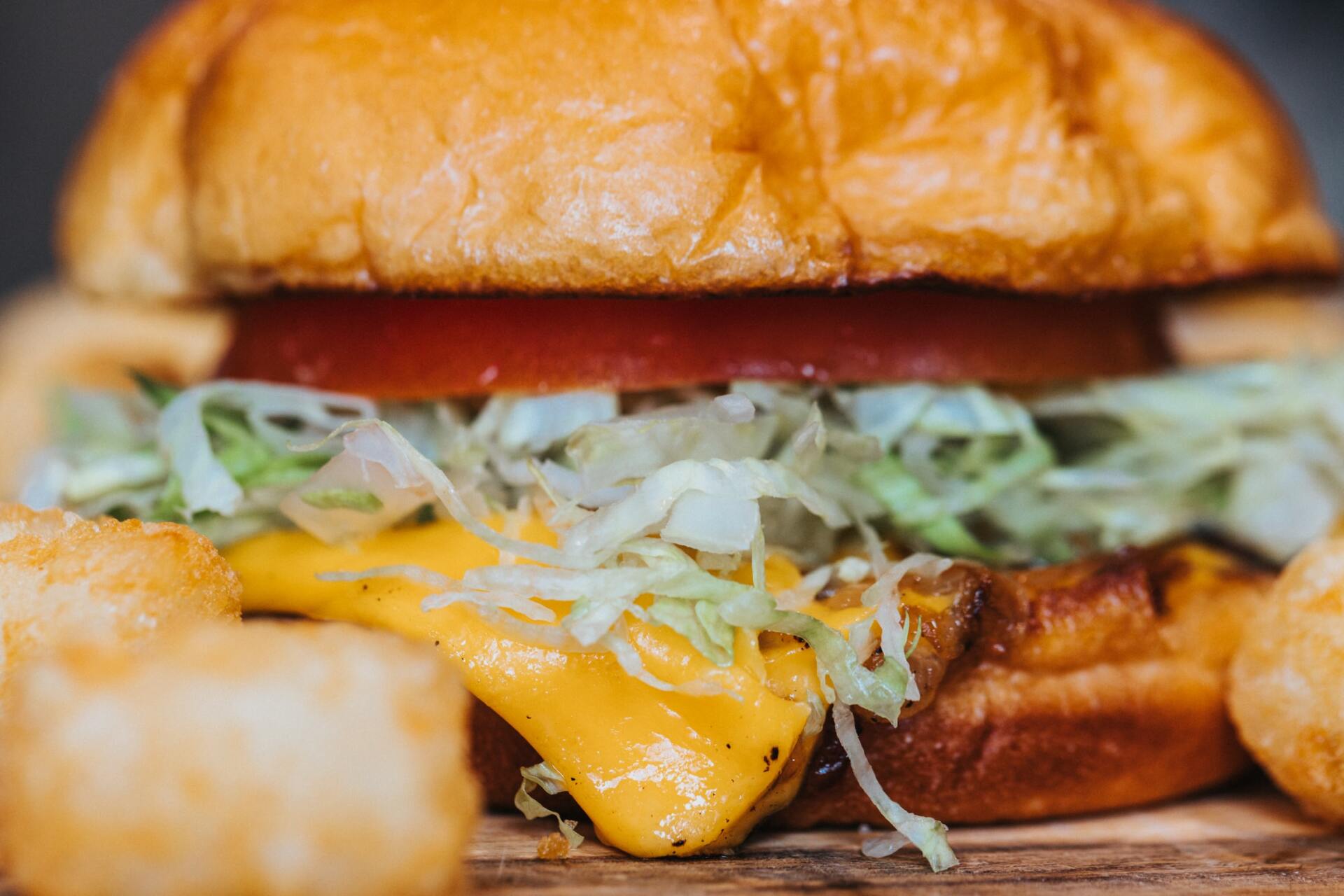 Cheeseburger with tomato and lettuce on a bun, with tater tots.