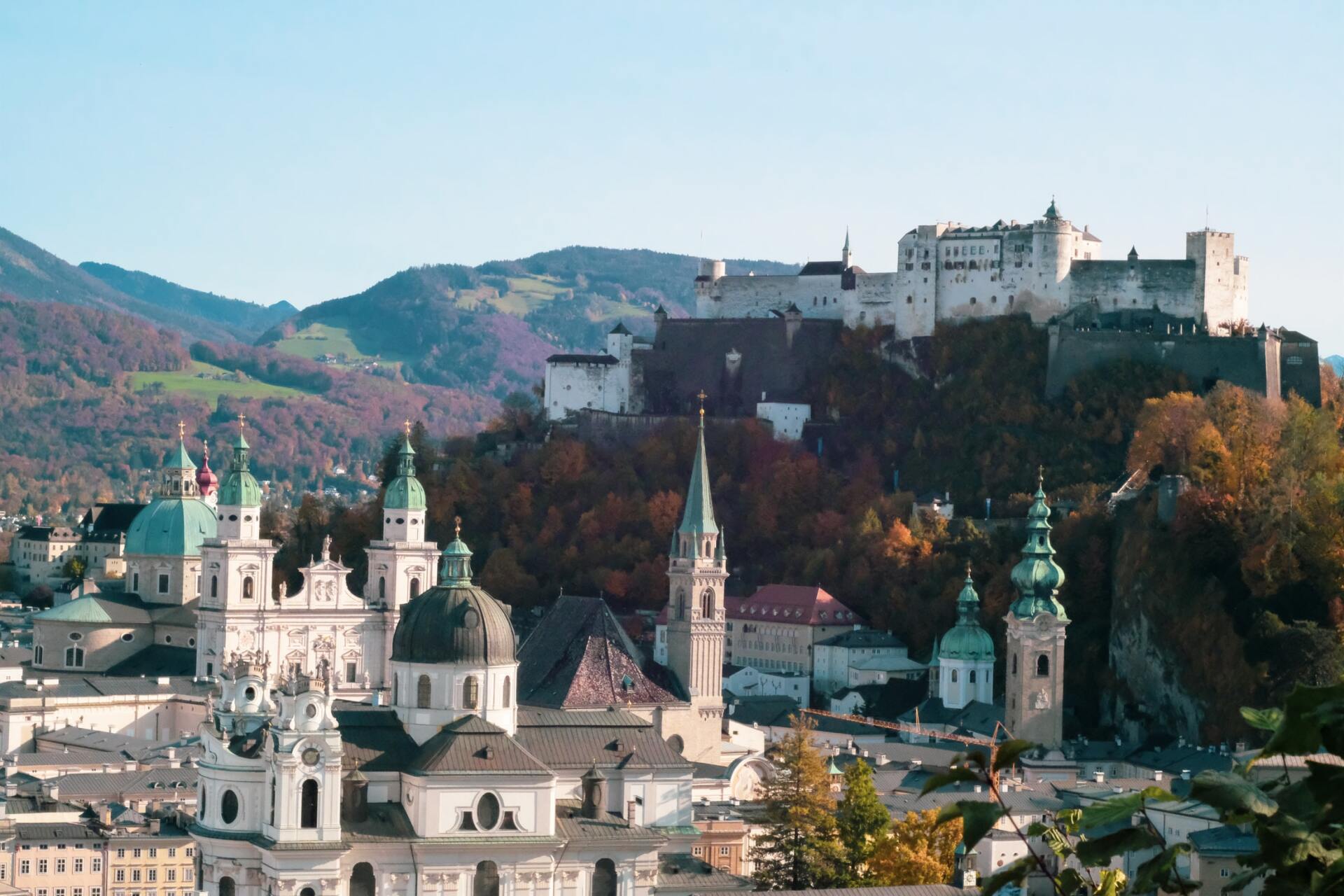 Weiße Kirche und Bergfestung über einer farbenprächtigen Herbststadt und Bergen