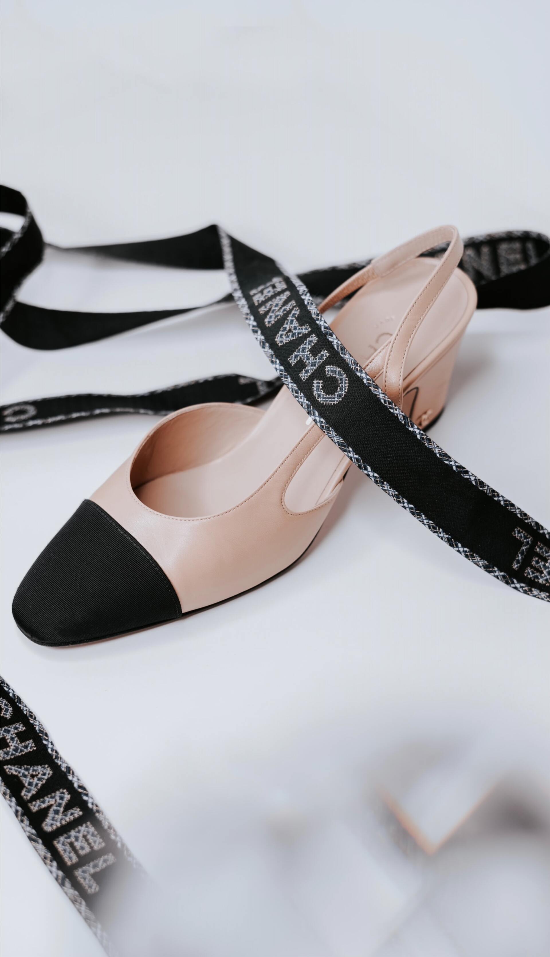 Beige and black Mary Jane flats with black ribbon straps on a white background