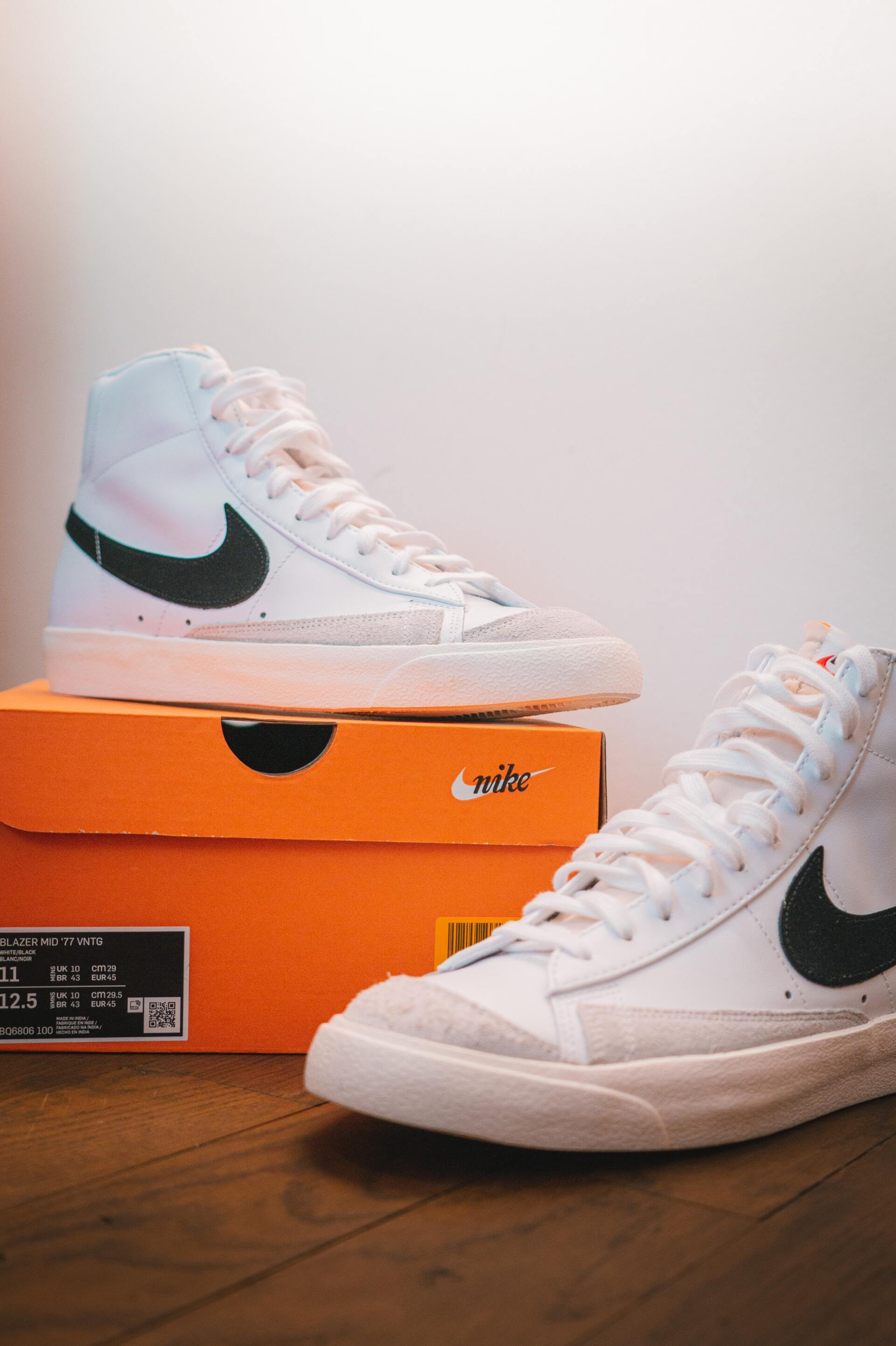White Nike high-top sneakers displayed on orange shoeboxes on a wooden floor