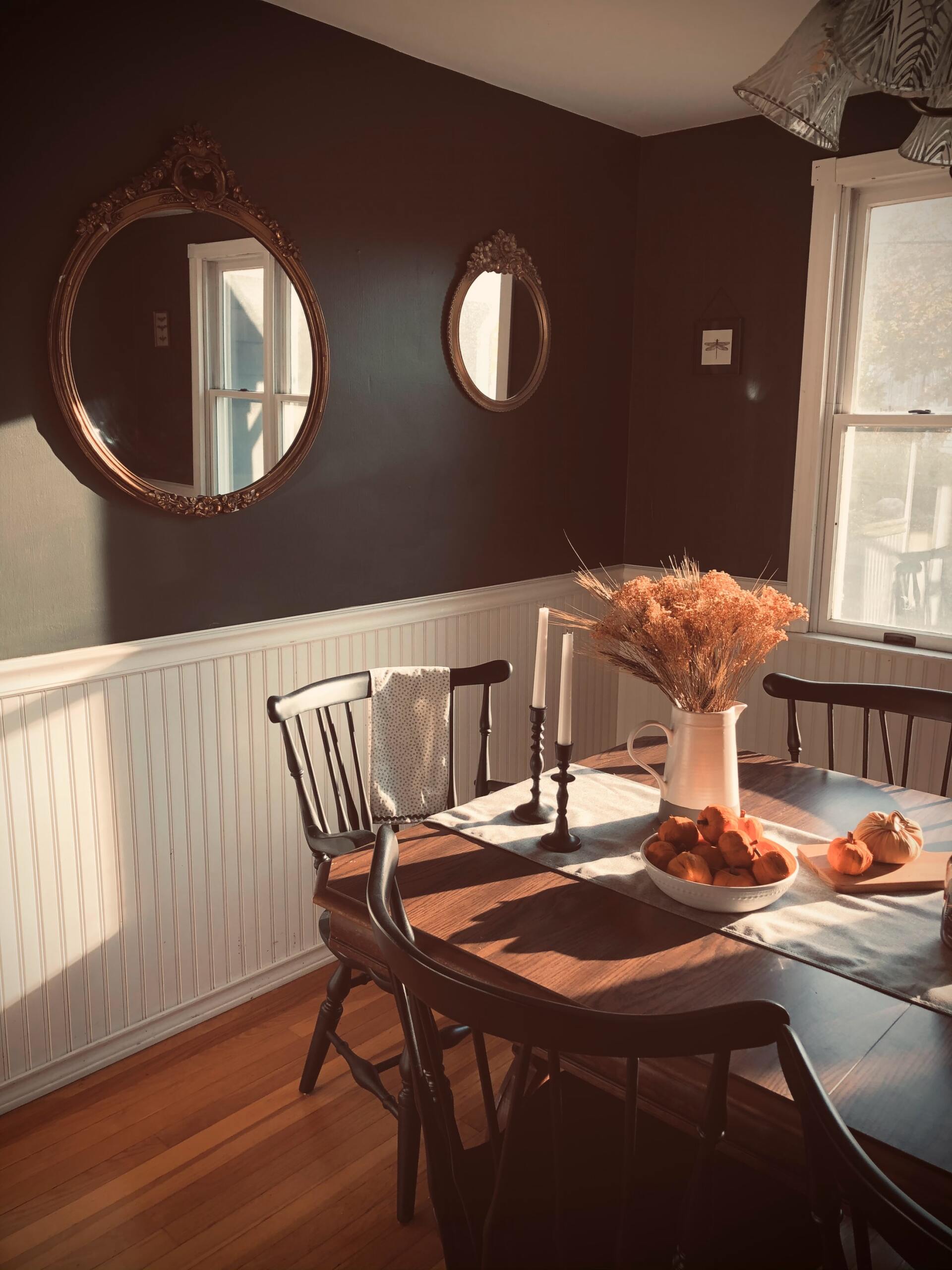 A dining room with a table and chairs and two mirrors