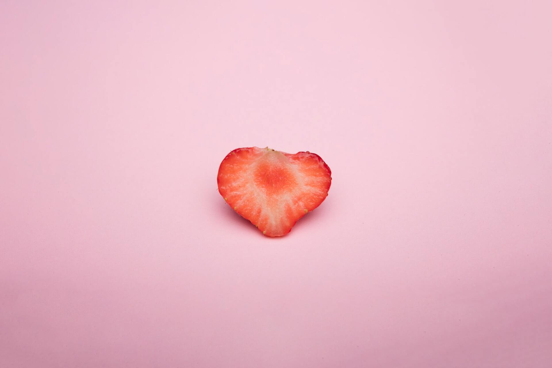Half of a strawberry, heart-shaped, on a pink background.