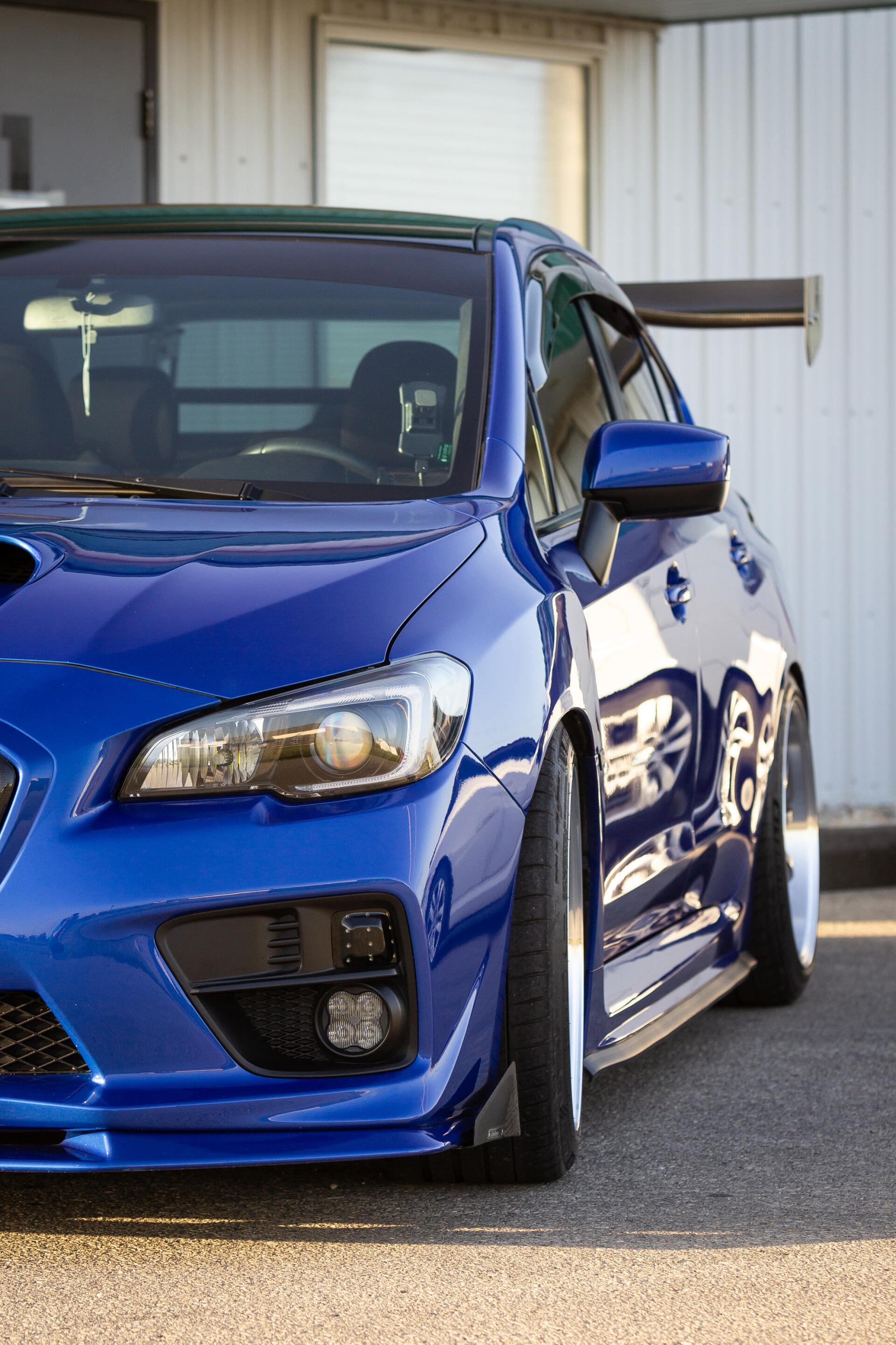 Blue Subaru WRX with a large wing, parked on a paved surface.