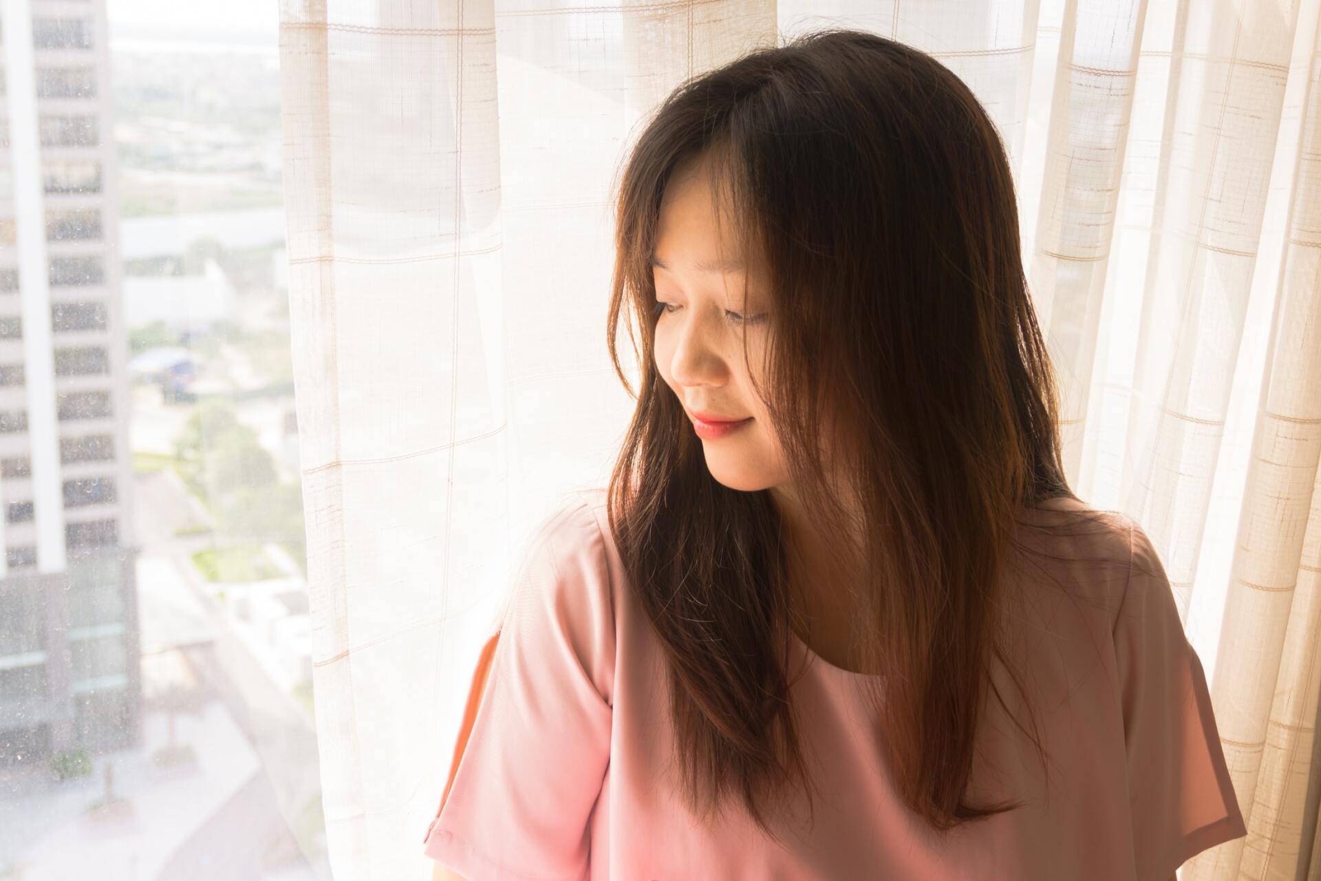 A woman is sitting in front of a window with her eyes closed.