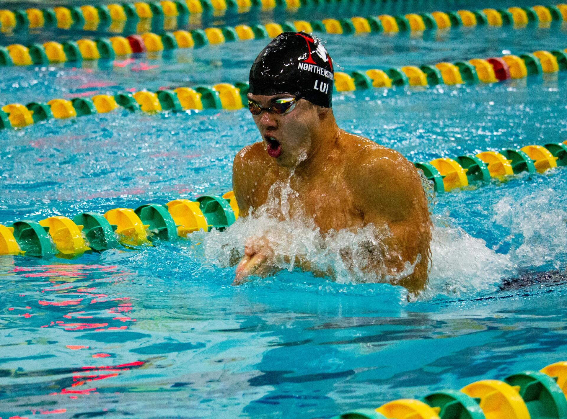 A man is swimming in a swimming pool with yellow and green lanes.