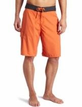 Man wearing orange board shorts with black waistband, standing barefoot against a white background