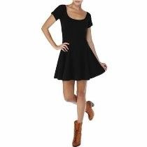 Woman in a black short-sleeve dress and brown boots posing against a white background