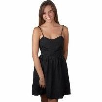 Woman in a black spaghetti-strap dress, standing and smiling against a white background