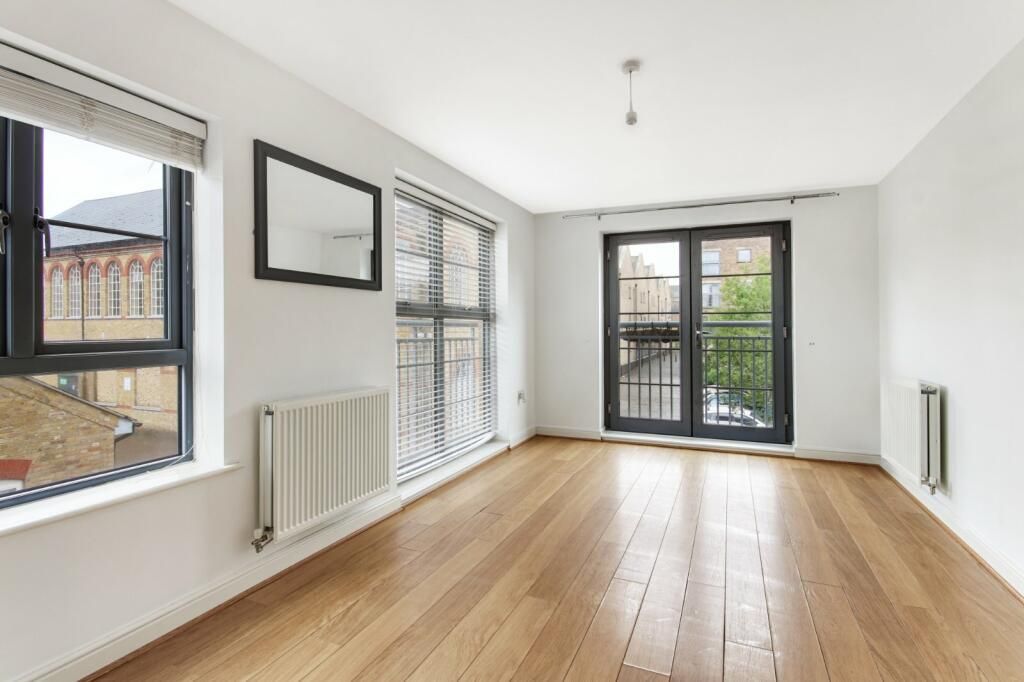 An empty living room with hardwood floors and two windows.