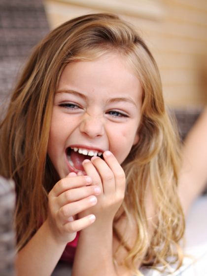 Smiling child laughing with hands near mouth in a softly lit indoor setting