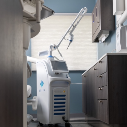 Modern dental clinic with a white treatment machine, overhead arm, and cabinets under bright window light