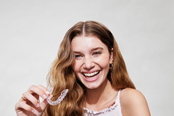 Smiling woman holding a clear aligner against a light gray background