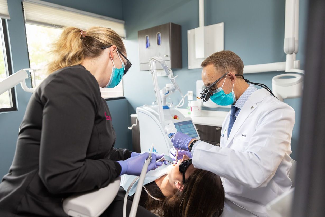 Dentist and assistant treating a patient in a modern dental clinic, both wearing masks and gloves