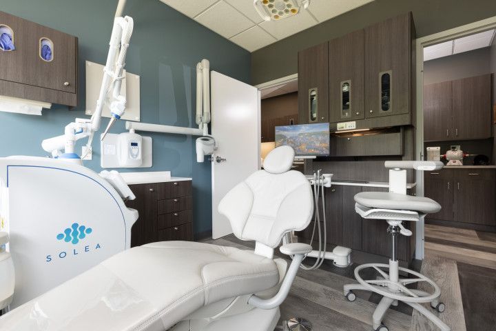 Modern dental exam room with chair, overhead light, cabinets, and equipment