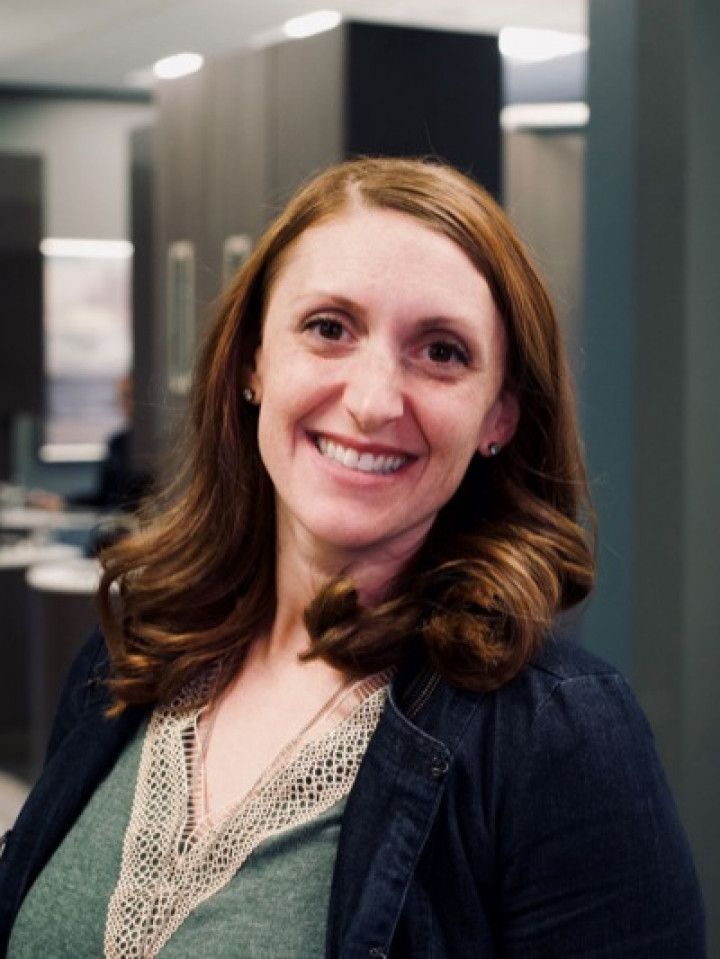 Smiling woman in a green top and dark cardigan standing indoors in an office setting