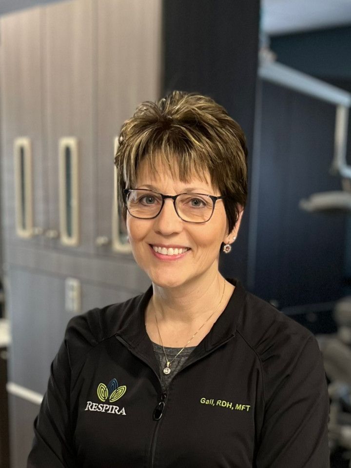 Smiling clinician in black scrubs with glasses, standing in a medical office hallway