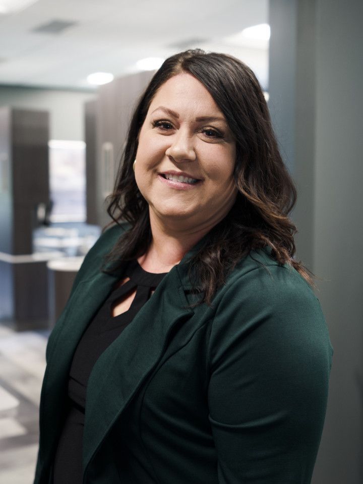 Smiling woman in a dark green blazer standing in an office hallway
