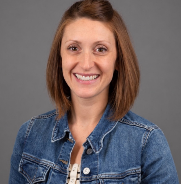 Smiling woman in a green top and dark cardigan standing indoors in an office setting