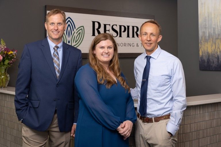 Three people posing indoors in business attire in front of a “Respira” sign.