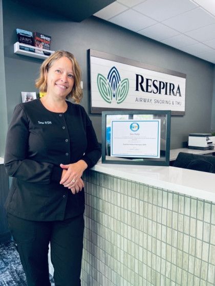 Woman standing at a clinic reception desk beside a Respira sign and framed certificate