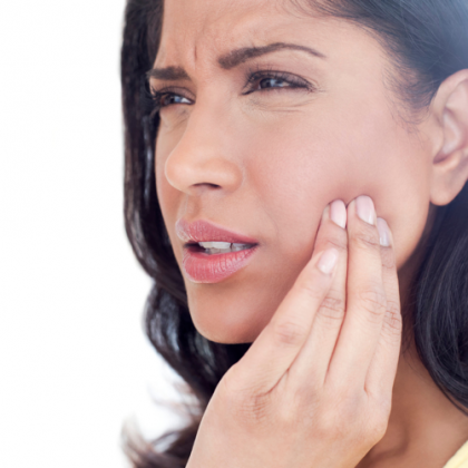 Woman touching her cheek with a pained expression, suggesting tooth or jaw pain.