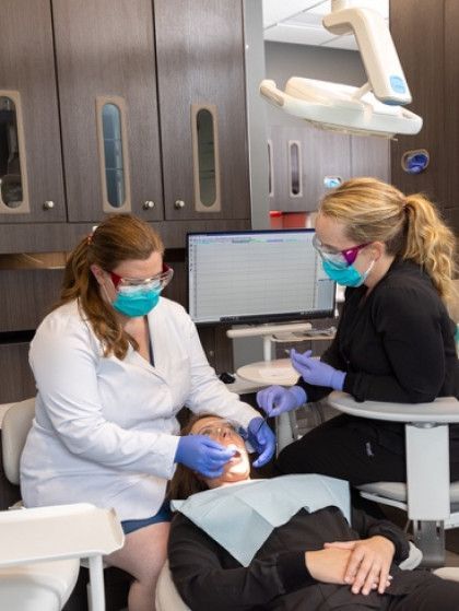 Dentist and assistant treating a patient in a dental office, wearing masks and gloves