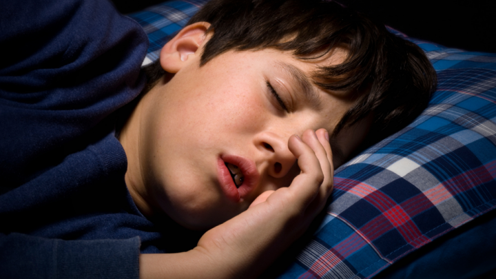 Sleeping child resting on a blue plaid pillow, hand over face.