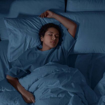 Person sleeping in bed under blue blankets, arm raised above head.