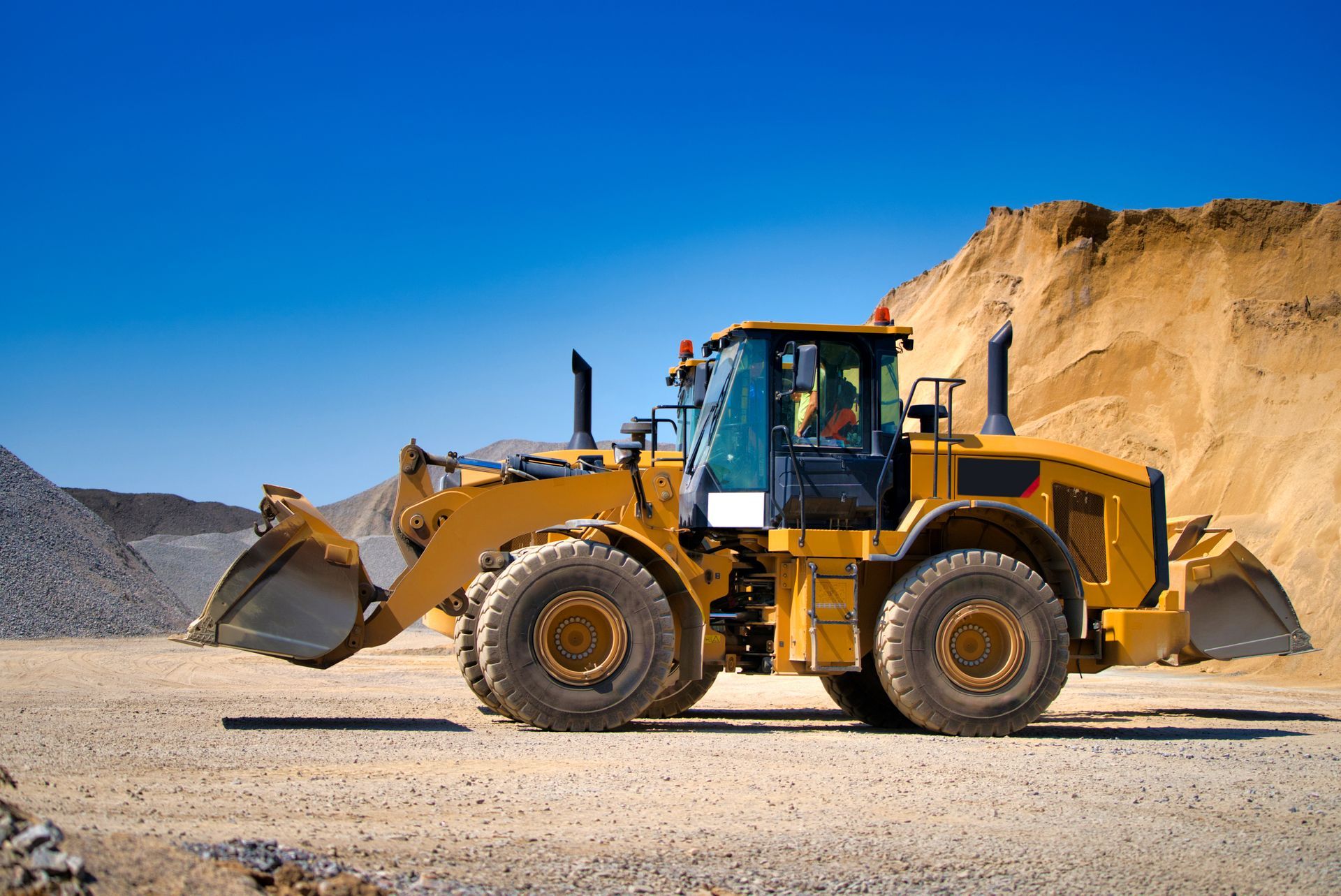 Yellow front loader digging dirt in a quarry under a clear blue sky