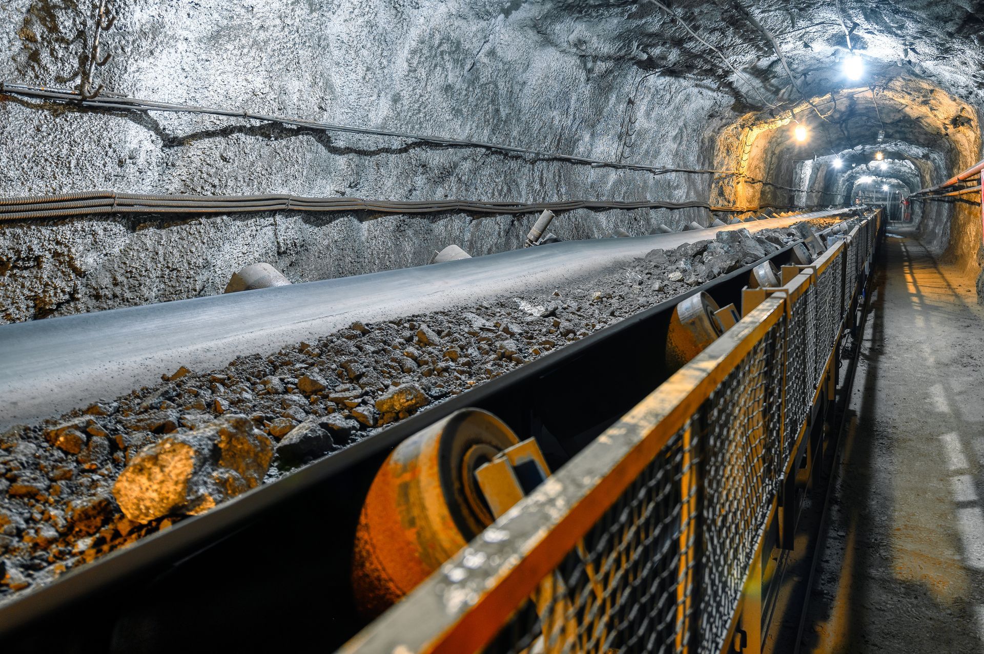 Closeup of belt conveyor transporting rocks and ores inside a mine.