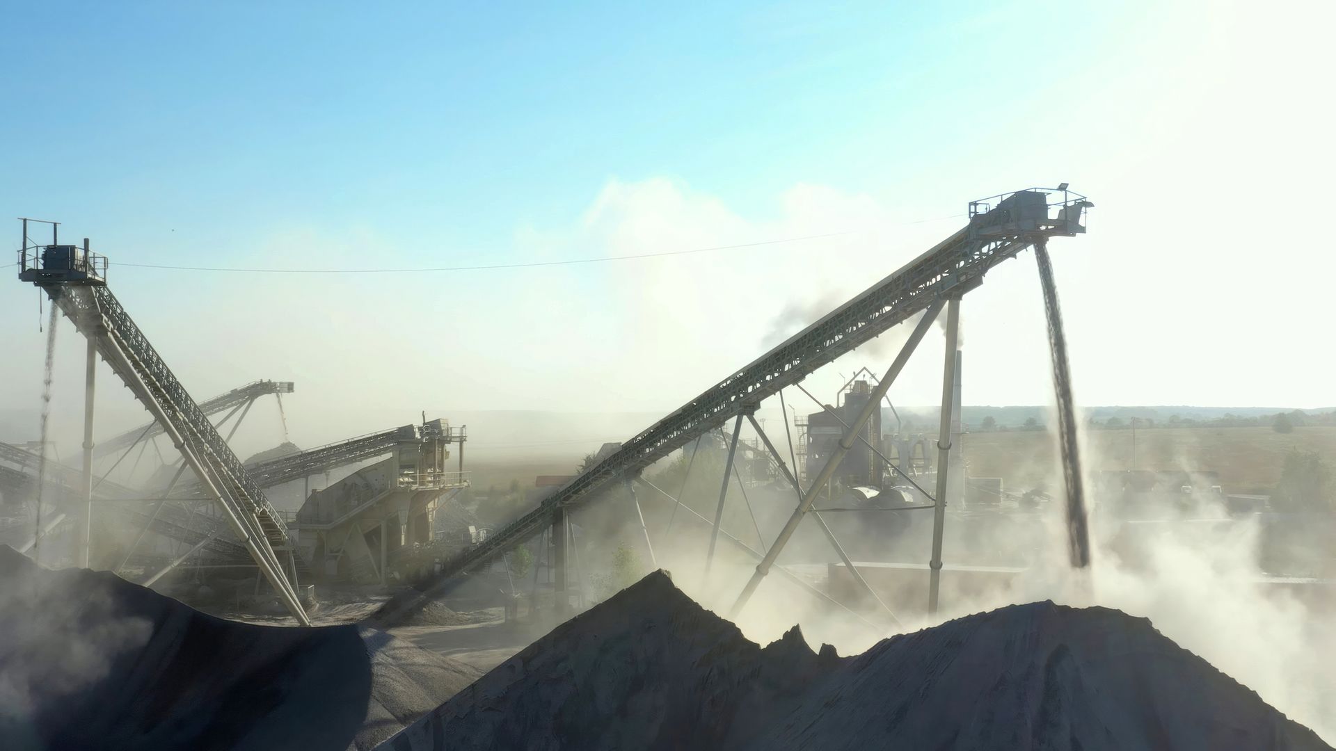 An industrial quarry with conveyors and machinery in a dusty setting.