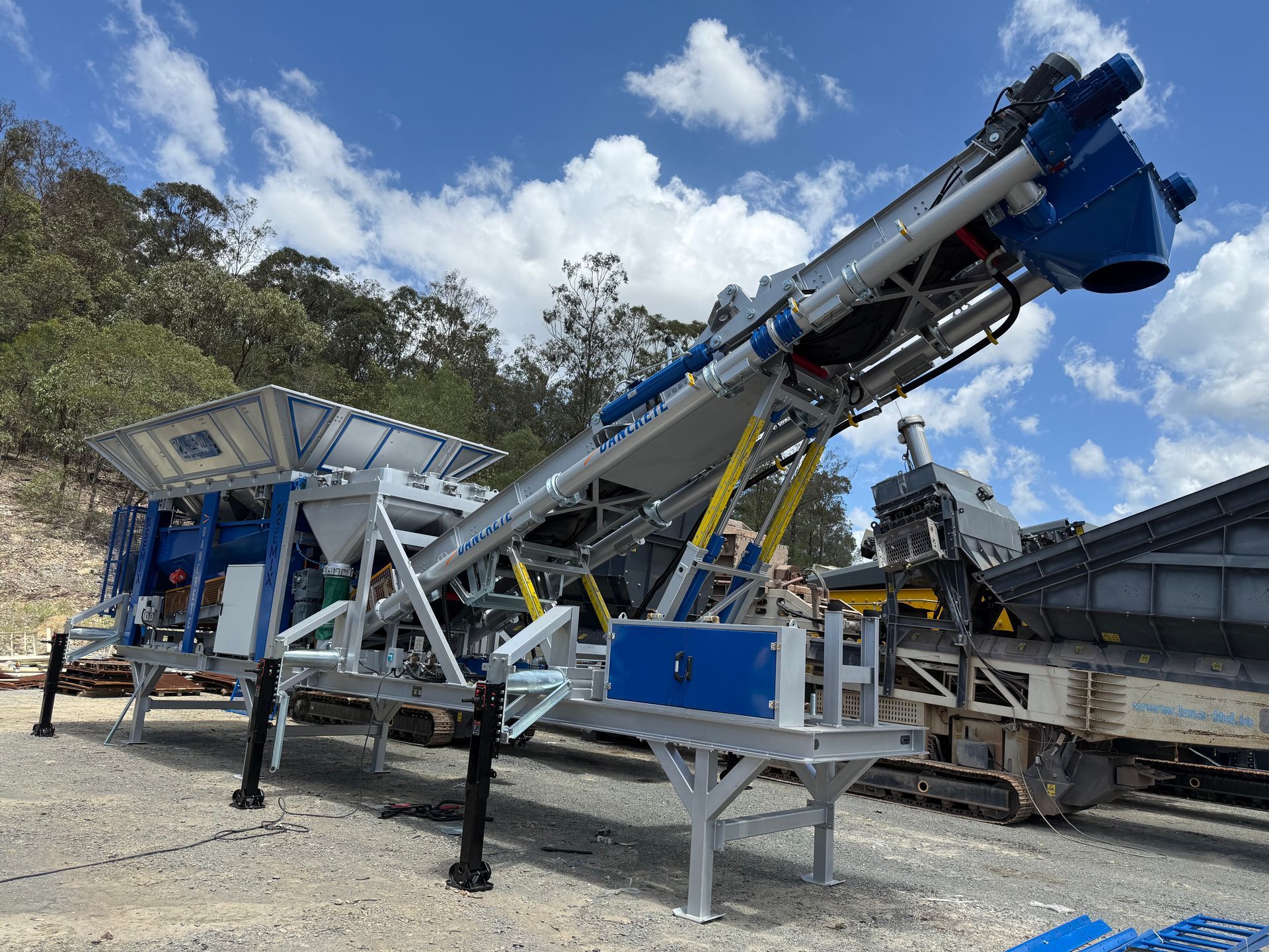 Blue and silver industrial machine with conveyor belt, outdoors against a cloudy sky.