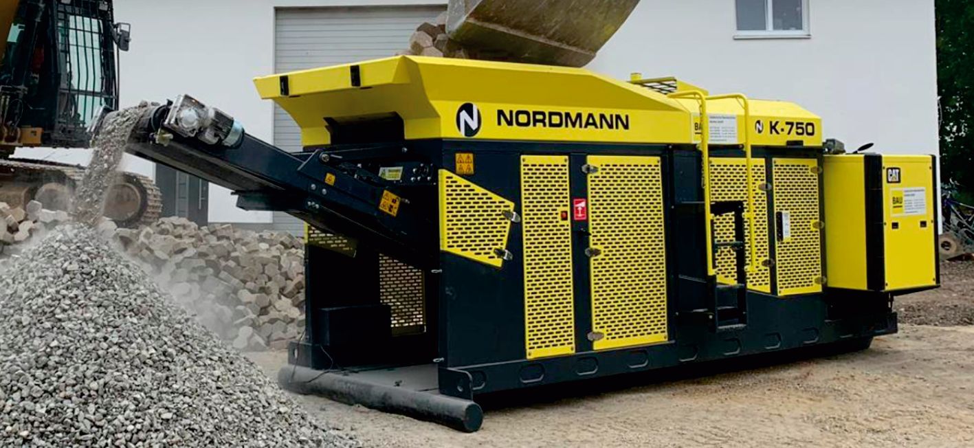 A yellow and black NORMANN CK 783 machine crushing rocks at a construction site. A pile of crushed gravel is in the foreground.