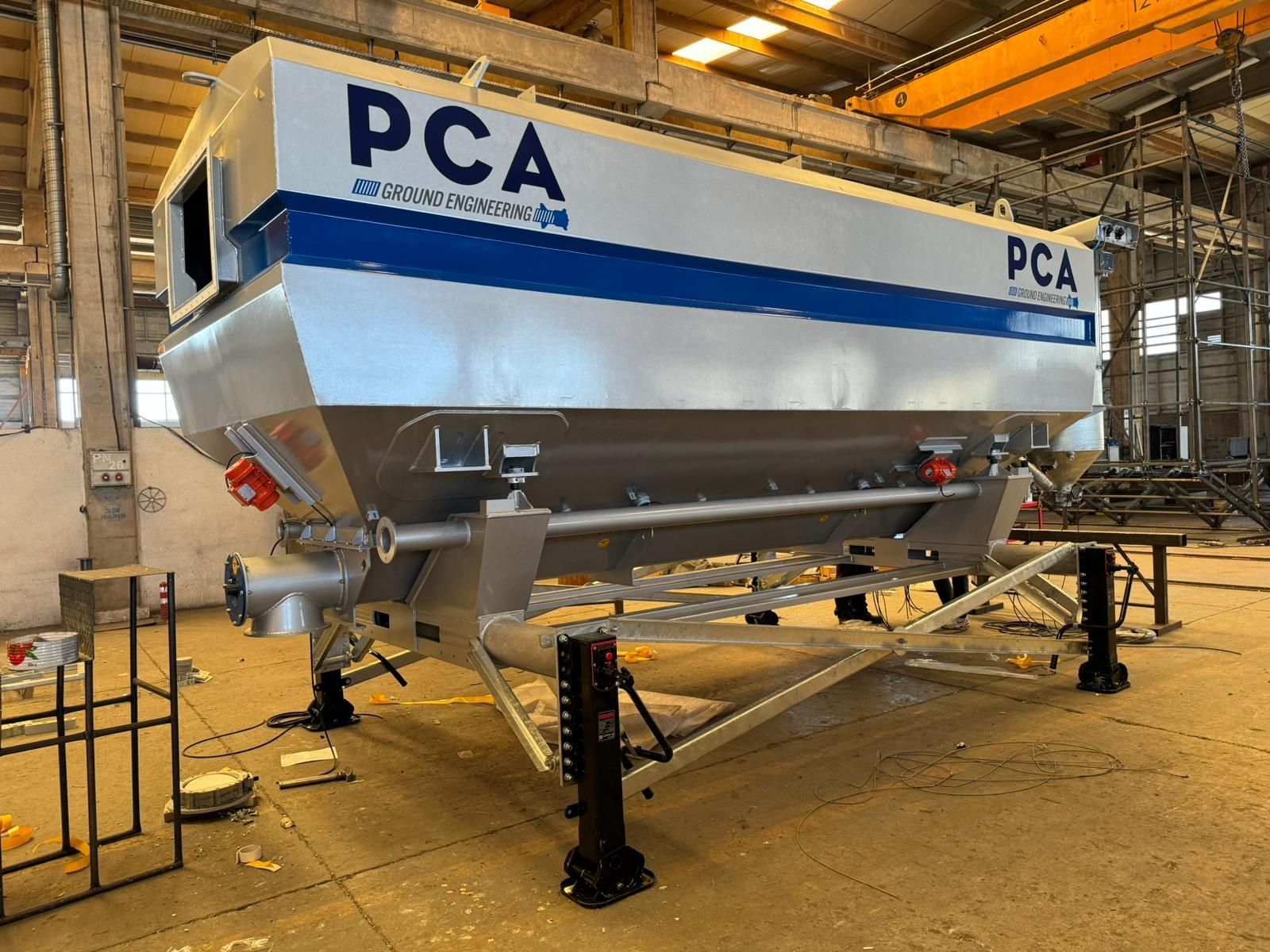 Large, industrial-looking silver and blue PCA hopper with support frame inside a factory.