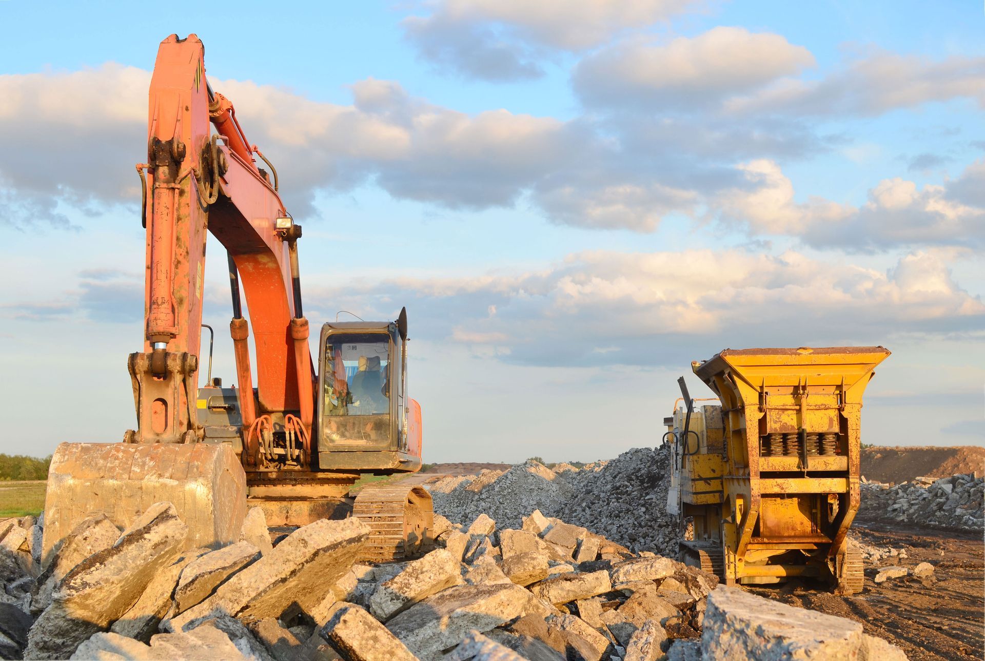 Excavator and rock crusher at construction site under cloudy sky.