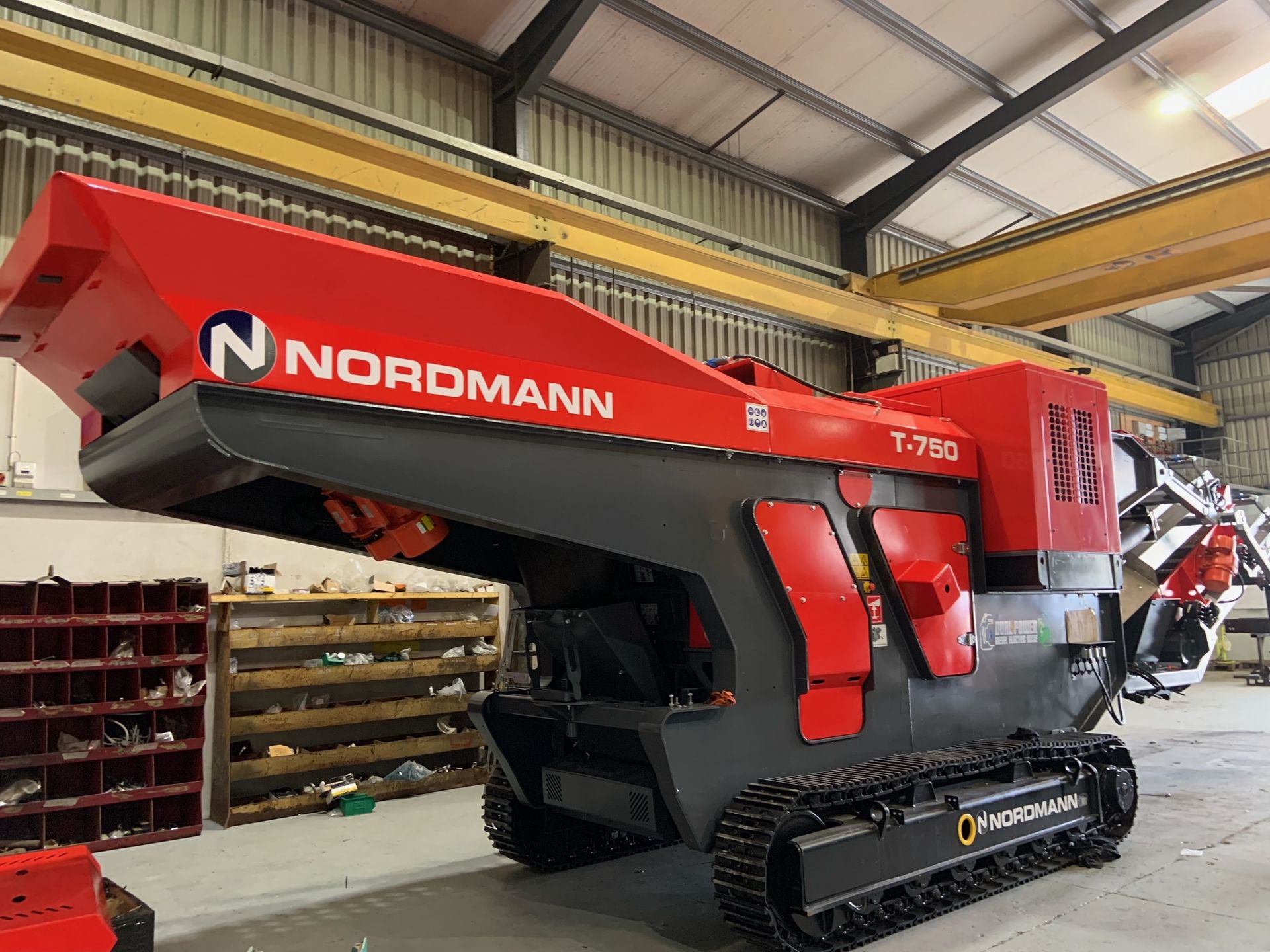 A red and black Nordmann T-2900 tracked shredder in a workshop. The machine has a large hopper and cutting mechanism visible.