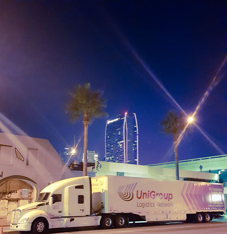 UniGroup moving truck parked at night near a lit city building and palm trees
