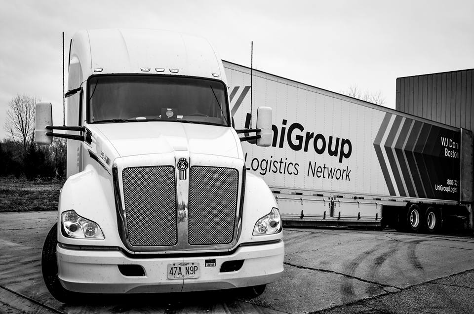 Black-and-white photo of a semi truck parked beside a logistics trailer in an industrial yard